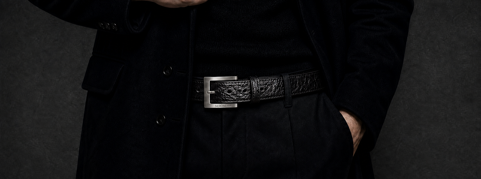 Person wearing a long black coat with a belt against a dark background